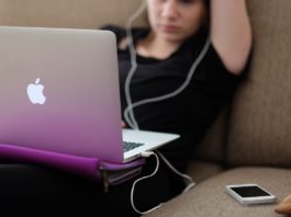 Une adolescente devant son ordinateur, avec écouteur aux oreilles et son smartphone sur le canapé à côté d'elle
