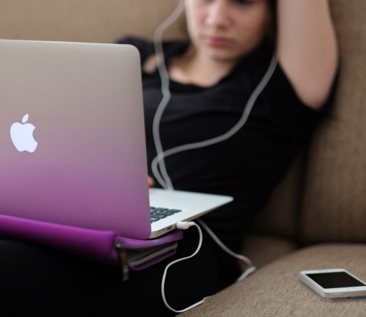 Une adolescente devant son ordinateur, avec écouteur aux oreilles et son smartphone sur le canapé à côté d'elle