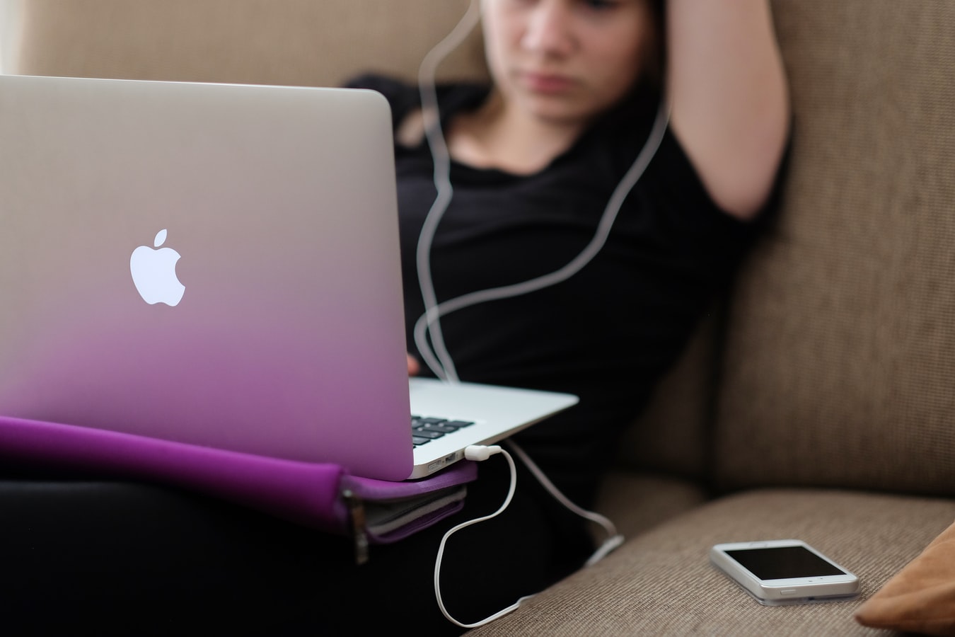 Une adolescente devant son ordinateur, avec écouteur aux oreilles et son smartphone sur le canapé à côté d'elle